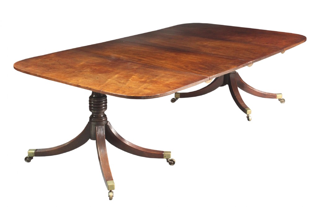 An antique mahogany twin pedestal dining table with rounded corners, reeded splayed legs, and brass castors.