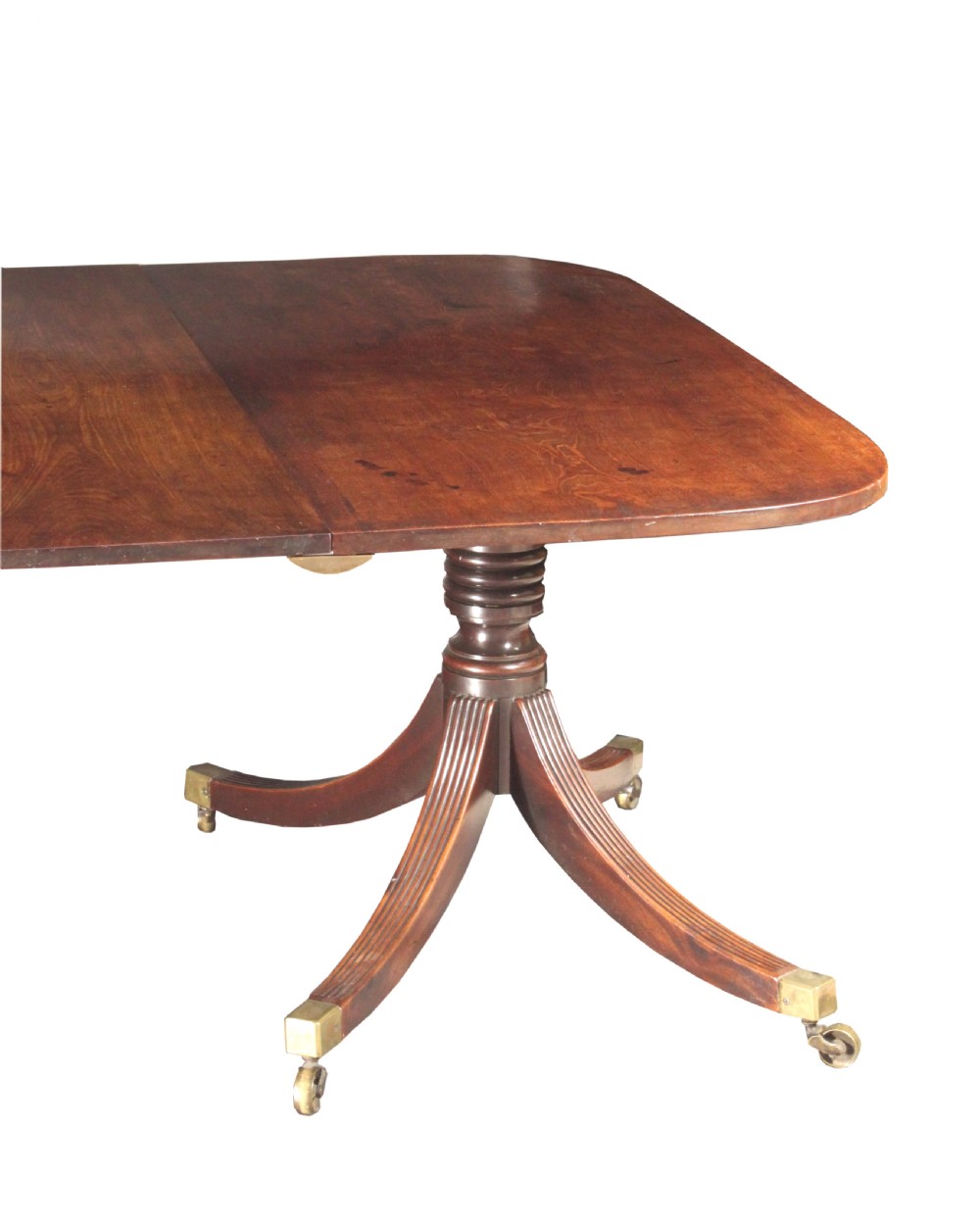 An antique mahogany twin pedestal dining table with rounded corners, reeded splayed legs, and brass castors. View IV