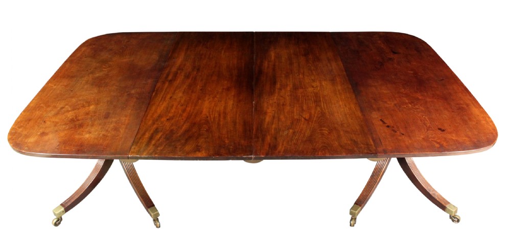 An antique mahogany twin pedestal dining table with rounded corners, reeded splayed legs, and brass castors. View V