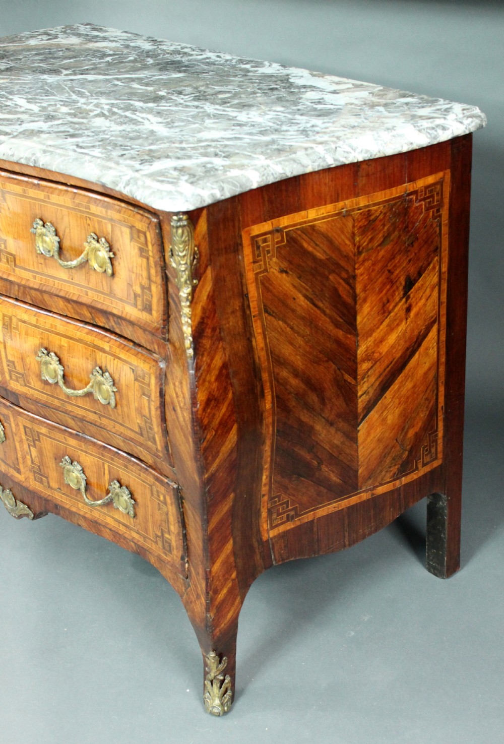 A Louis XV style kingwood commode featuring three drawers with geometric parquetry inlay, gilt bronze mounts, and a shaped grey marble top. View VIII