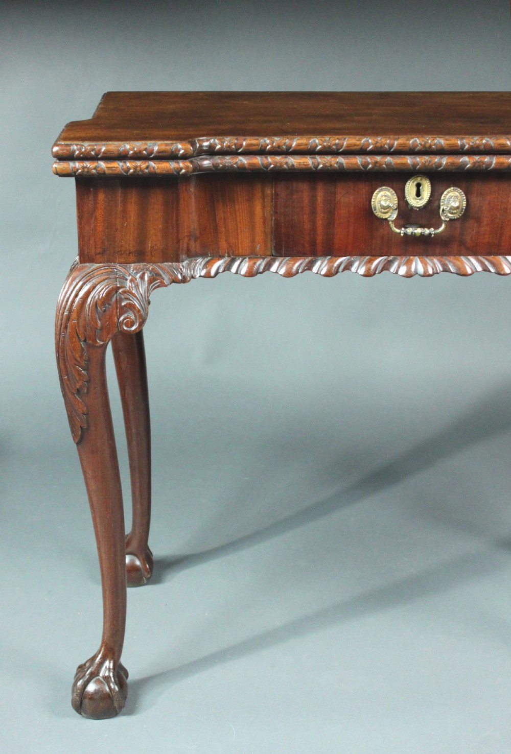 An antique Chippendale mahogany fold-over card table with cabriole legs, carved ball and claw feet, and a single drawer with brass hardware. View V