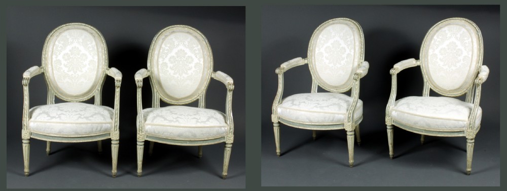A set of four antique French Louis XVI fauteuil armchairs with painted distressed frames, oval medallion backs, padded armrests, fluted legs, and cream patterned upholstery.