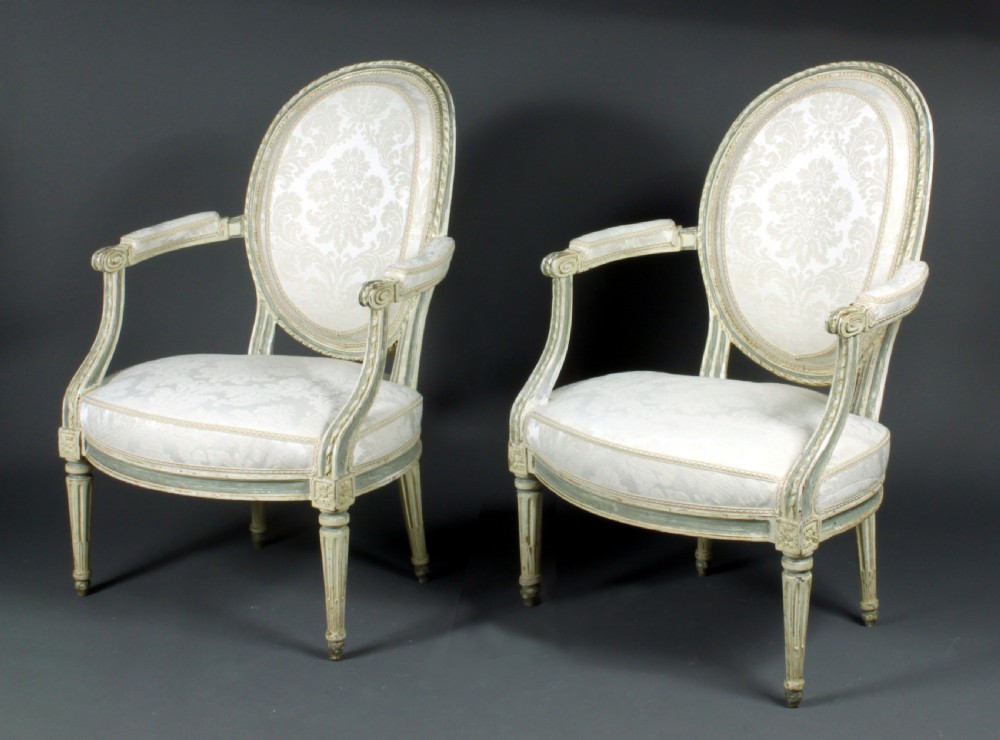 A set of four antique French Louis XVI fauteuil armchairs with painted distressed frames, oval medallion backs, padded armrests, fluted legs, and cream patterned upholstery. View II