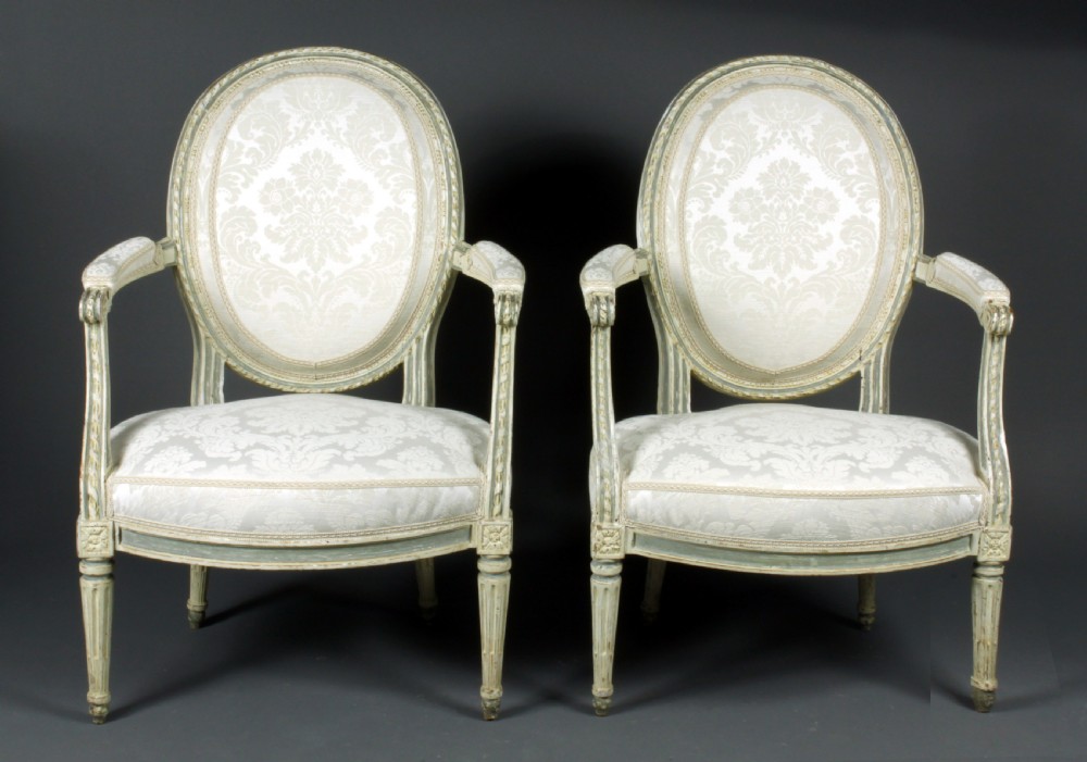 A set of four antique French Louis XVI fauteuil armchairs with painted distressed frames, oval medallion backs, padded armrests, fluted legs, and cream patterned upholstery. View III