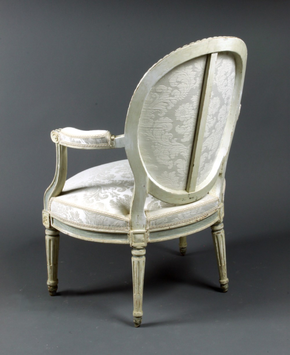 A set of four antique French Louis XVI fauteuil armchairs with painted distressed frames, oval medallion backs, padded armrests, fluted legs, and cream patterned upholstery. View V