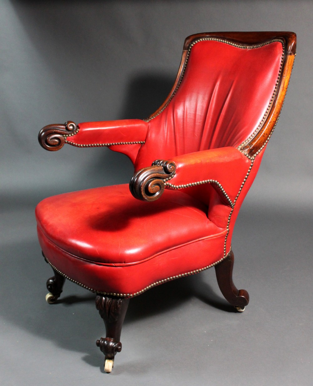 A Victorian red leather armchair with carved mahogany frame, brass studding, scroll armrests, and castors.