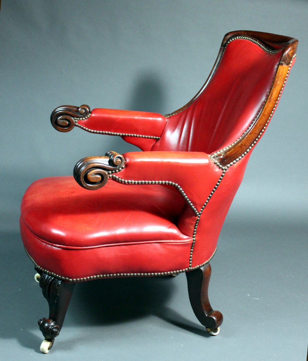 A Victorian red leather armchair with carved mahogany frame, brass studding, scroll armrests, and castors. View II