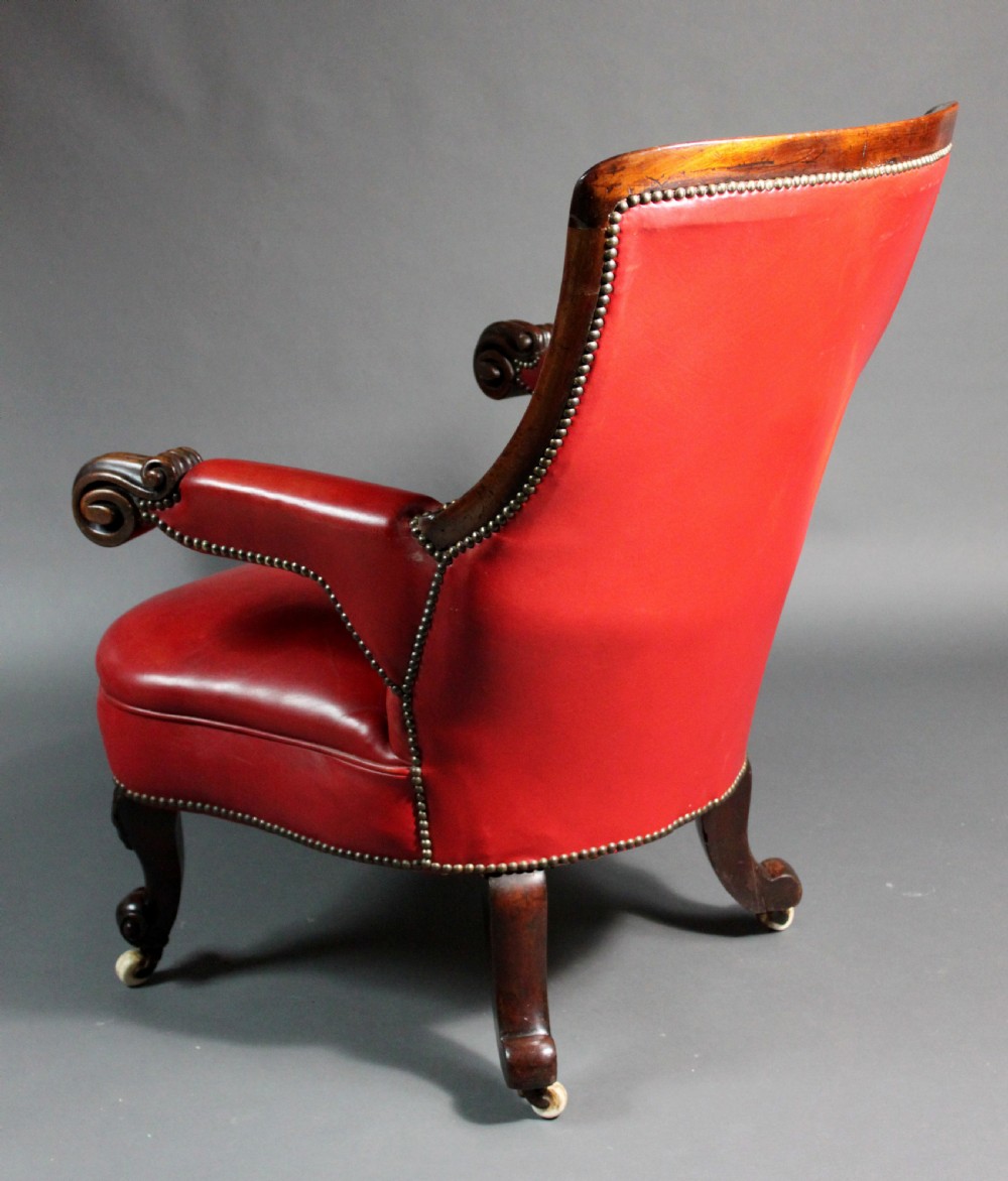 A Victorian red leather armchair with carved mahogany frame, brass studding, scroll armrests, and castors. View III