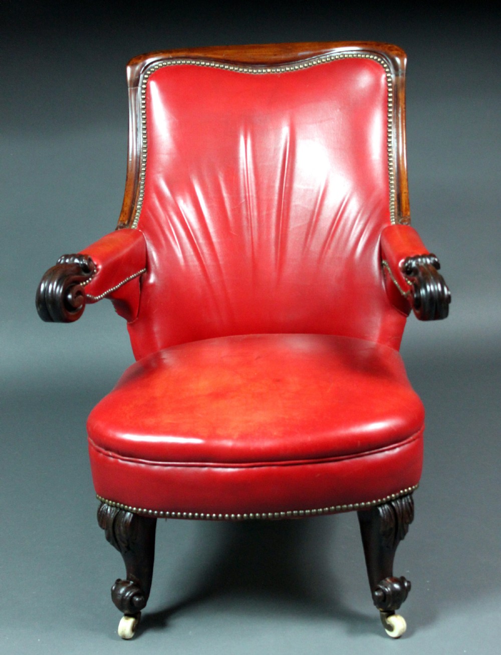 A Victorian red leather armchair with carved mahogany frame, brass studding, scroll armrests, and castors. View IV