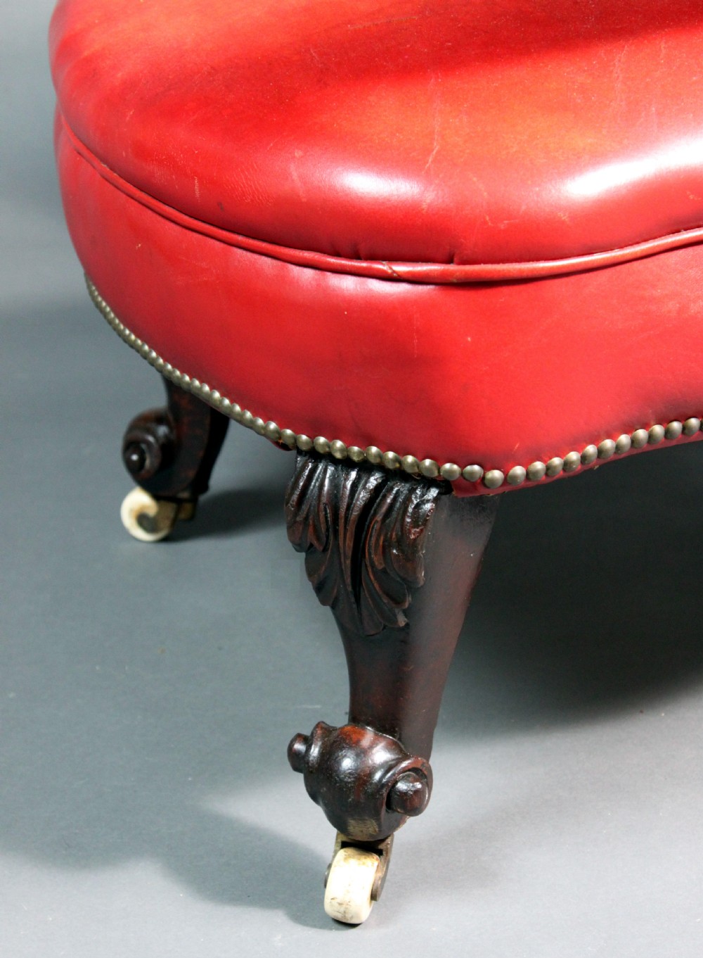 A Victorian red leather armchair with carved mahogany frame, brass studding, scroll armrests, and castors. View VI