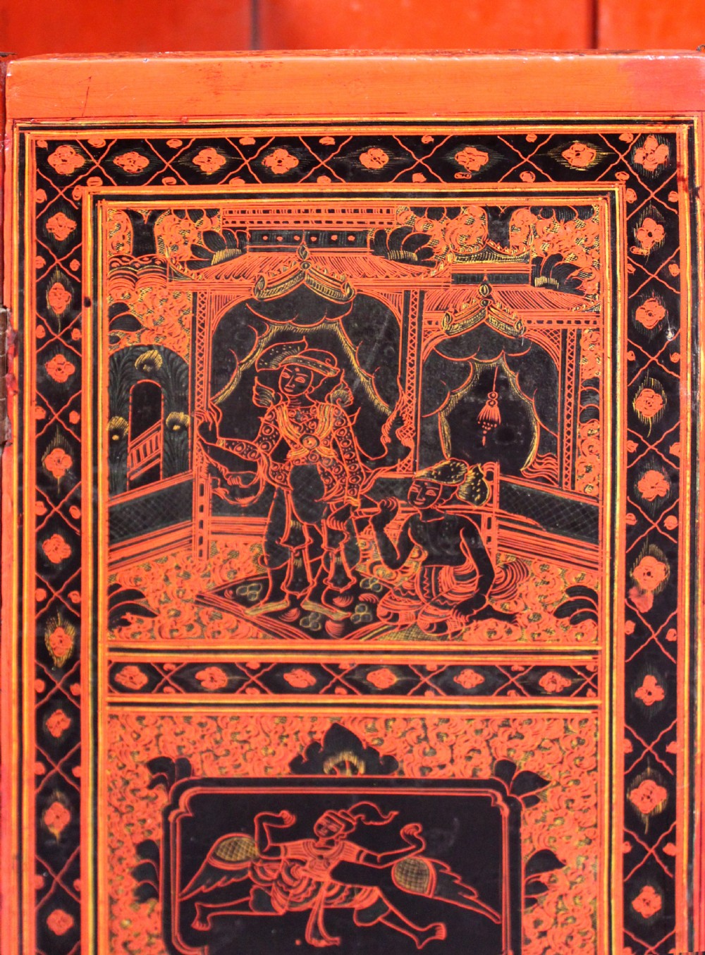 An octagonal red lacquer side table decorated with black hand-painted figures, elephants, and geometric borders. View V
