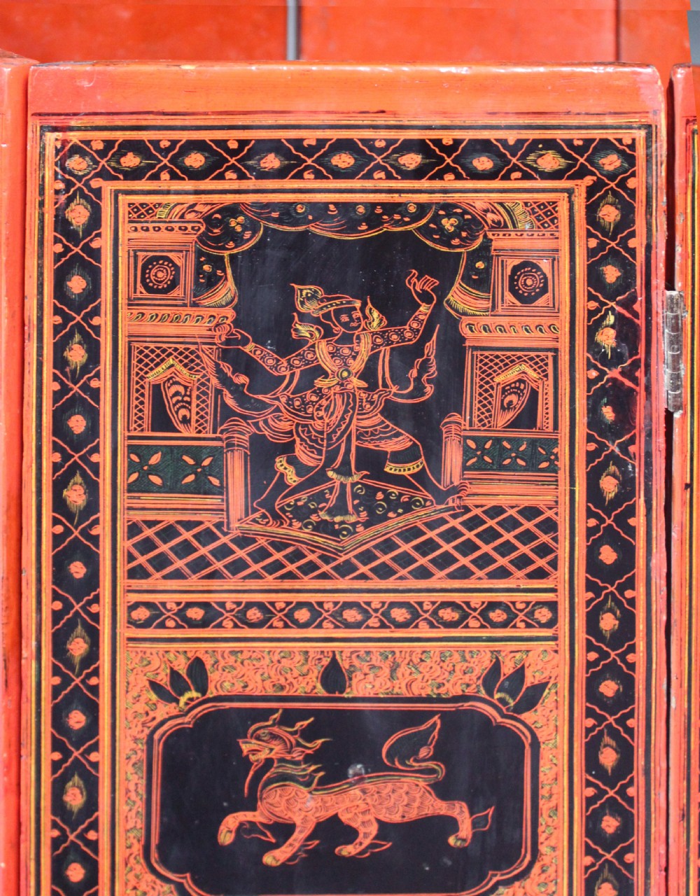 An octagonal red lacquer side table decorated with black hand-painted figures, elephants, and geometric borders. View VI