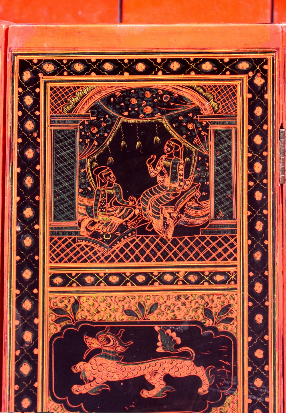 An octagonal red lacquer side table decorated with black hand-painted figures, elephants, and geometric borders. View VII