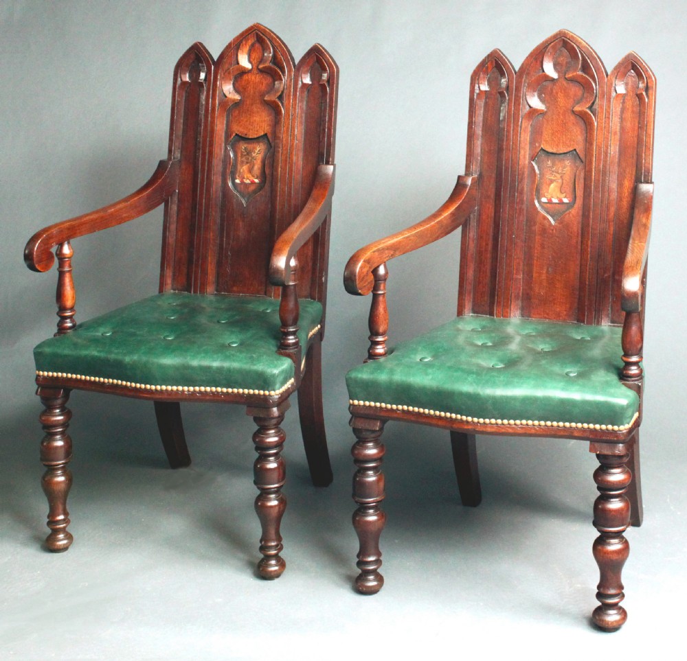 A pair of carved dark oak Gothic Revival hall armchairs featuring pointed arch backrests with painted armorial crests and green leather seats. View II