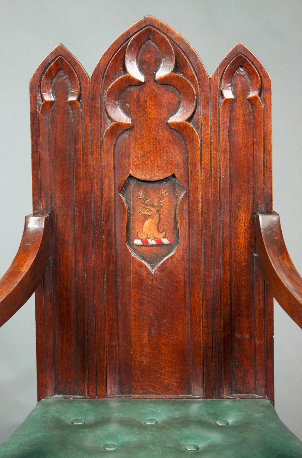 A pair of carved dark oak Gothic Revival hall armchairs featuring pointed arch backrests with painted armorial crests and green leather seats. View III