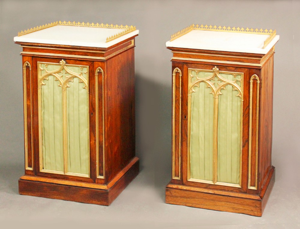 A pair of dark rosewood Regency Gothic pedestal cupboards featuring white marble tops with pierced brass galleries and pleated green silk doors framed by gilt tracery.