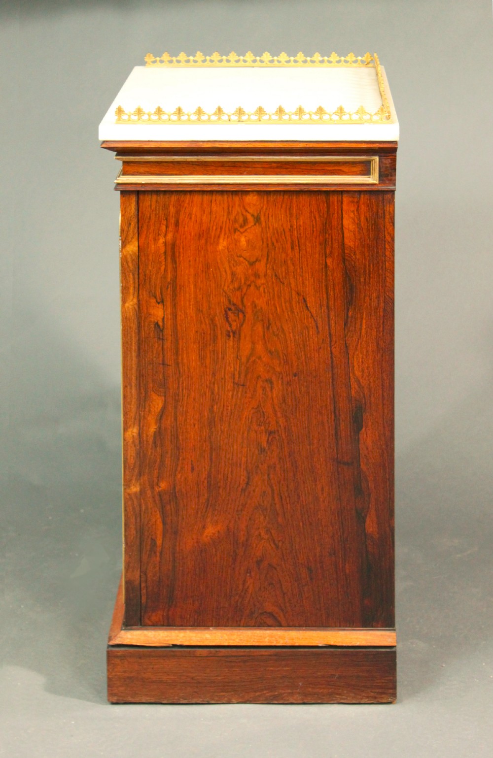 A pair of dark rosewood Regency Gothic pedestal cupboards featuring white marble tops with pierced brass galleries and pleated green silk doors framed by gilt tracery. View V