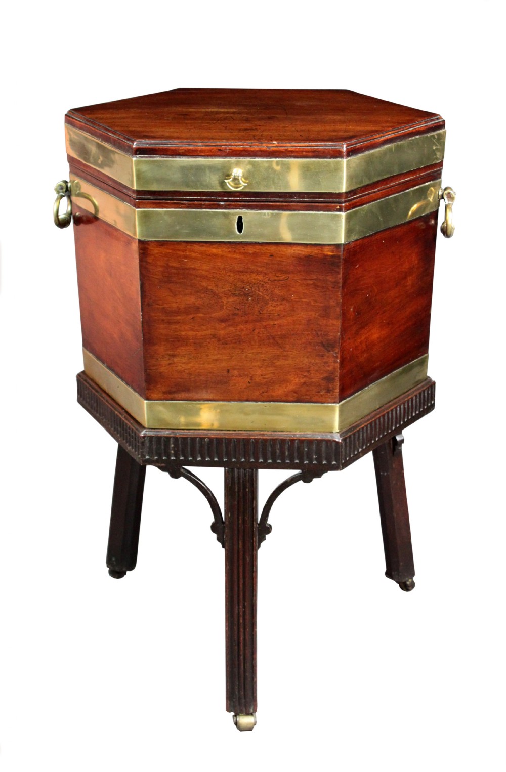 A hexagonal mahogany wine cooler featuring polished brass bands, side handles, and a fitted stand with fluted legs and brass castors.