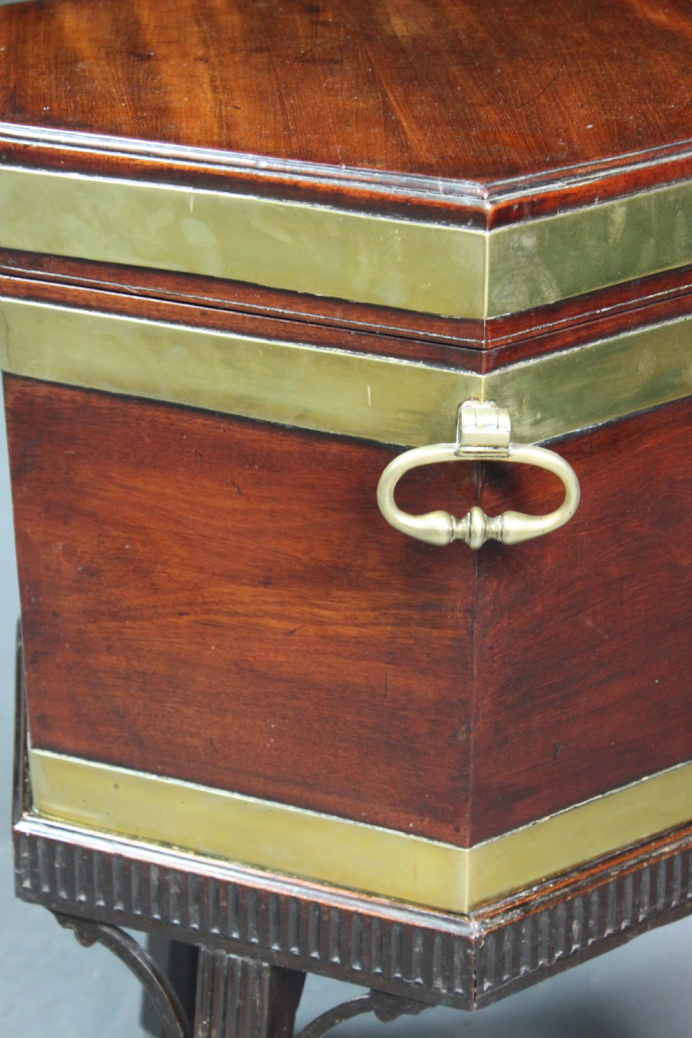 A hexagonal mahogany wine cooler featuring polished brass bands, side handles, and a fitted stand with fluted legs and brass castors. View III