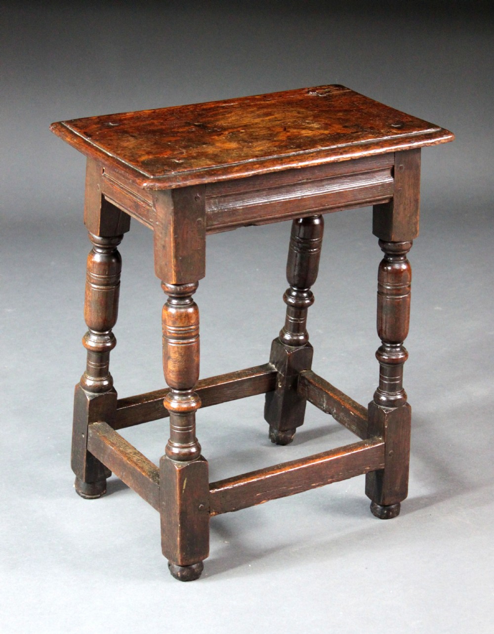 A seventeenth-century dark oak joined stool with turned legs, perimeter stretchers, and a moulded rectangular top.
