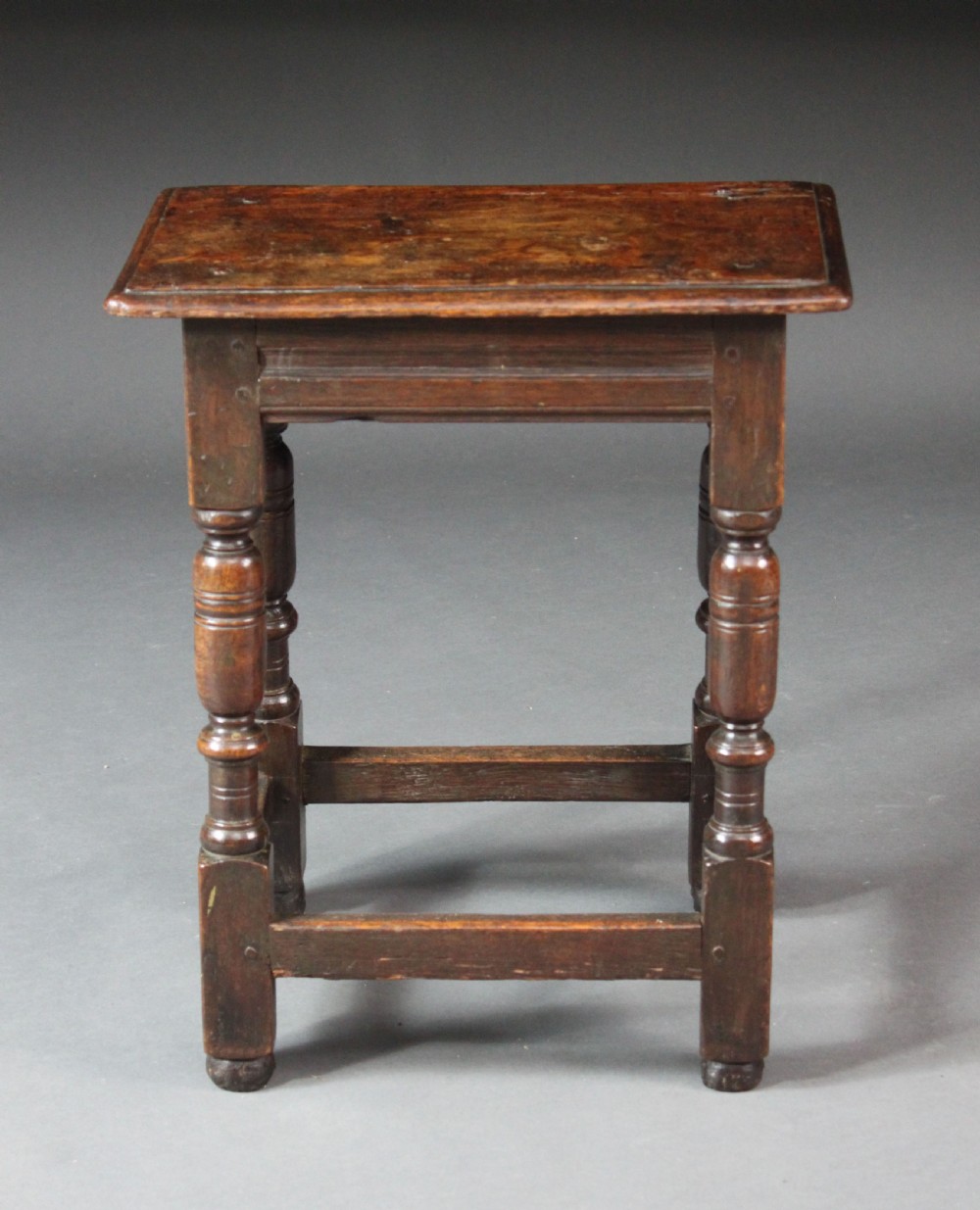 A seventeenth-century dark oak joined stool with turned legs, perimeter stretchers, and a moulded rectangular top. View II
