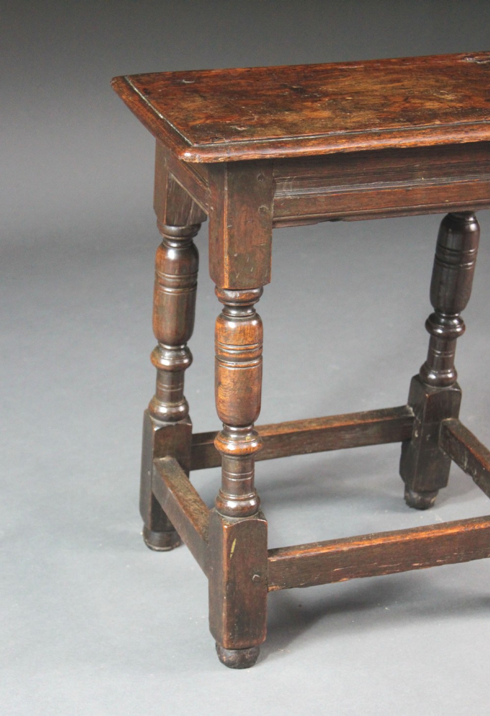 A seventeenth-century dark oak joined stool with turned legs, perimeter stretchers, and a moulded rectangular top. View IV