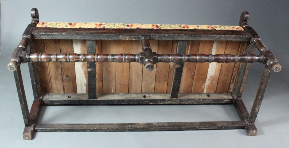 A late seventeenth-century dark carved oak settle featuring three carved back panels with floral motifs, turned legs, stretchers, and a floral patterned seat cushion. View VII