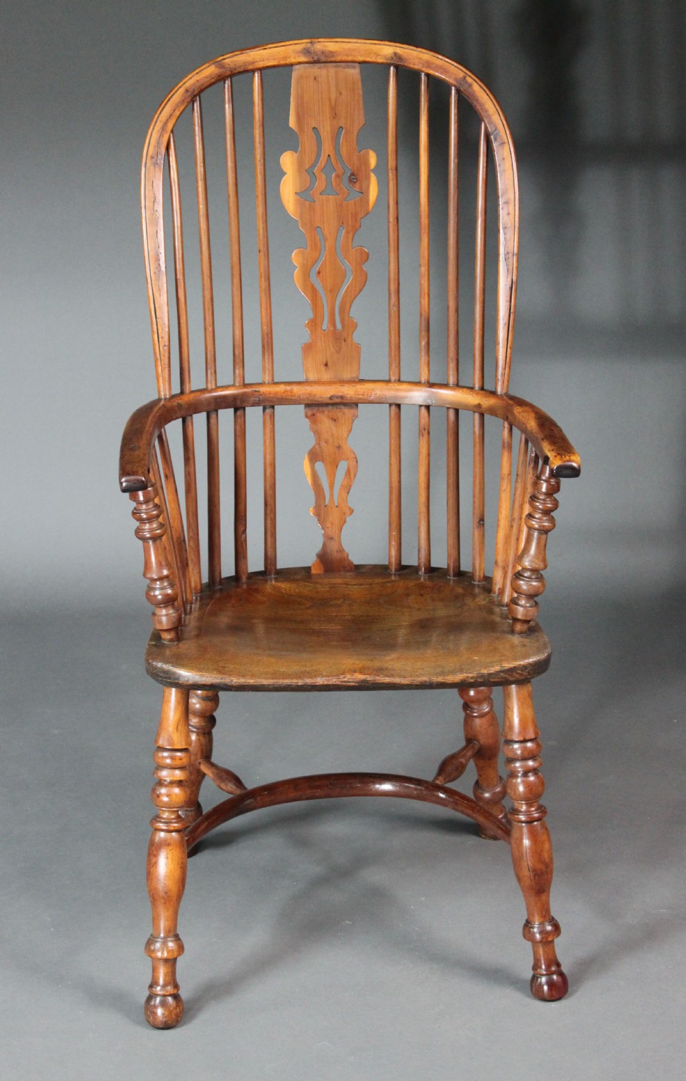 An antique high-back yew wood Windsor armchair featuring a pierced decorative splat, spindle backrest, turned legs, and a curved crinoline stretcher.