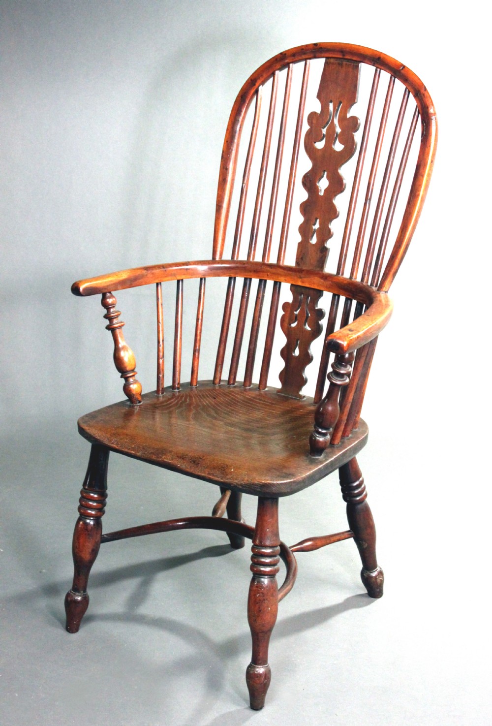 An antique yew wood Windsor armchair featuring a high bow back with vertical spindles, a pierced central splat, turned arm supports, and a shaped seat. View III