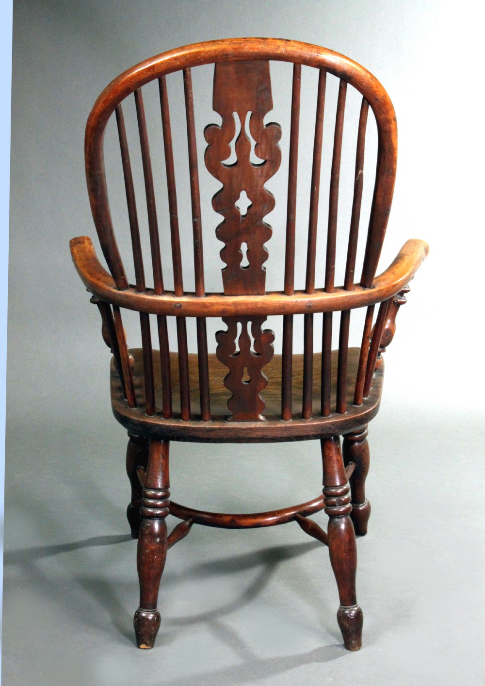 An antique yew wood Windsor armchair featuring a high bow back with vertical spindles, a pierced central splat, turned arm supports, and a shaped seat. View V