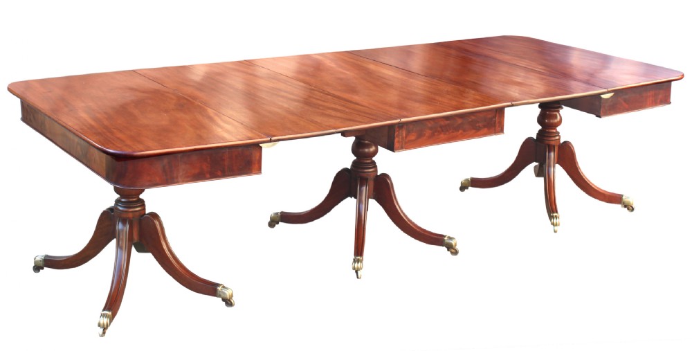 A long Regency-style mahogany extension dining table featuring three turned pedestal bases on brass cap castors.
