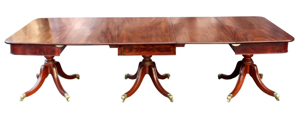 A long Regency-style mahogany extension dining table featuring three turned pedestal bases on brass cap castors. View II