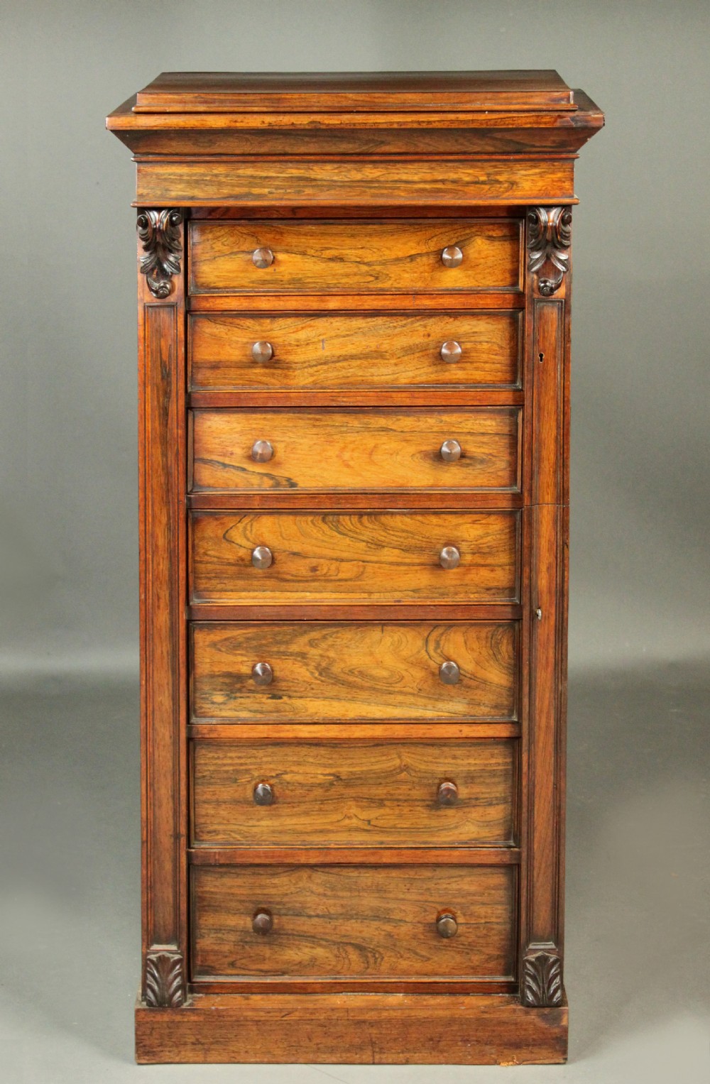 A tall, narrow Victorian rosewood Wellington chest featuring seven stacked drawers with wooden knob handles and a hinged side locking bar. View II