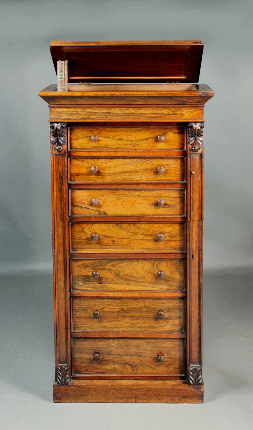 A tall, narrow Victorian rosewood Wellington chest featuring seven stacked drawers with wooden knob handles and a hinged side locking bar. View III