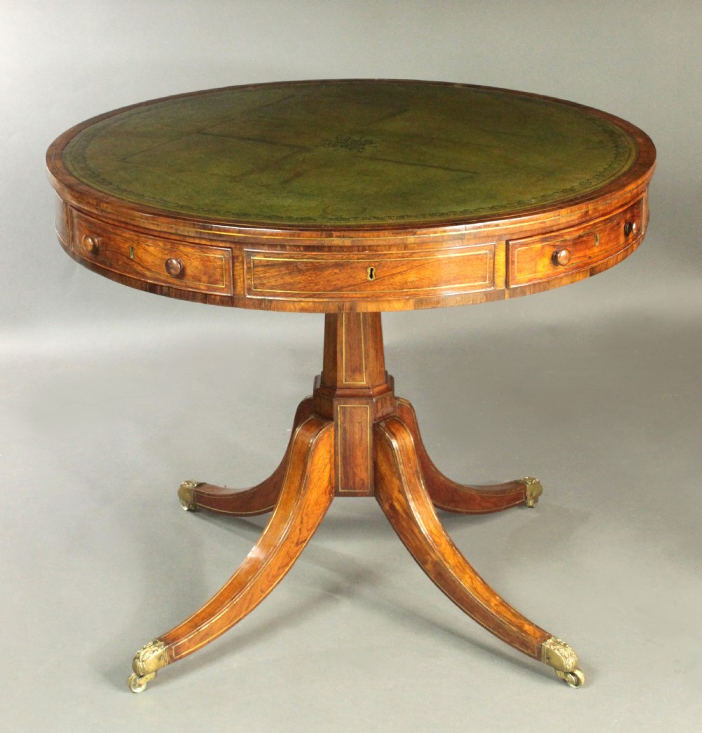 A circular Regency rosewood drum table with a green leather top, frieze drawers, and a central pedestal resting on four splayed legs with brass castors.