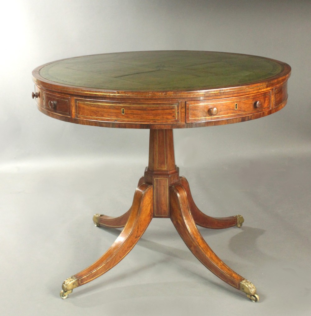 A circular Regency rosewood drum table with a green leather top, frieze drawers, and a central pedestal resting on four splayed legs with brass castors. View II