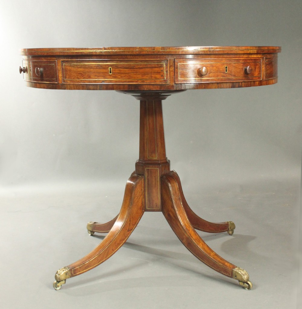 A circular Regency rosewood drum table with a green leather top, frieze drawers, and a central pedestal resting on four splayed legs with brass castors. View III