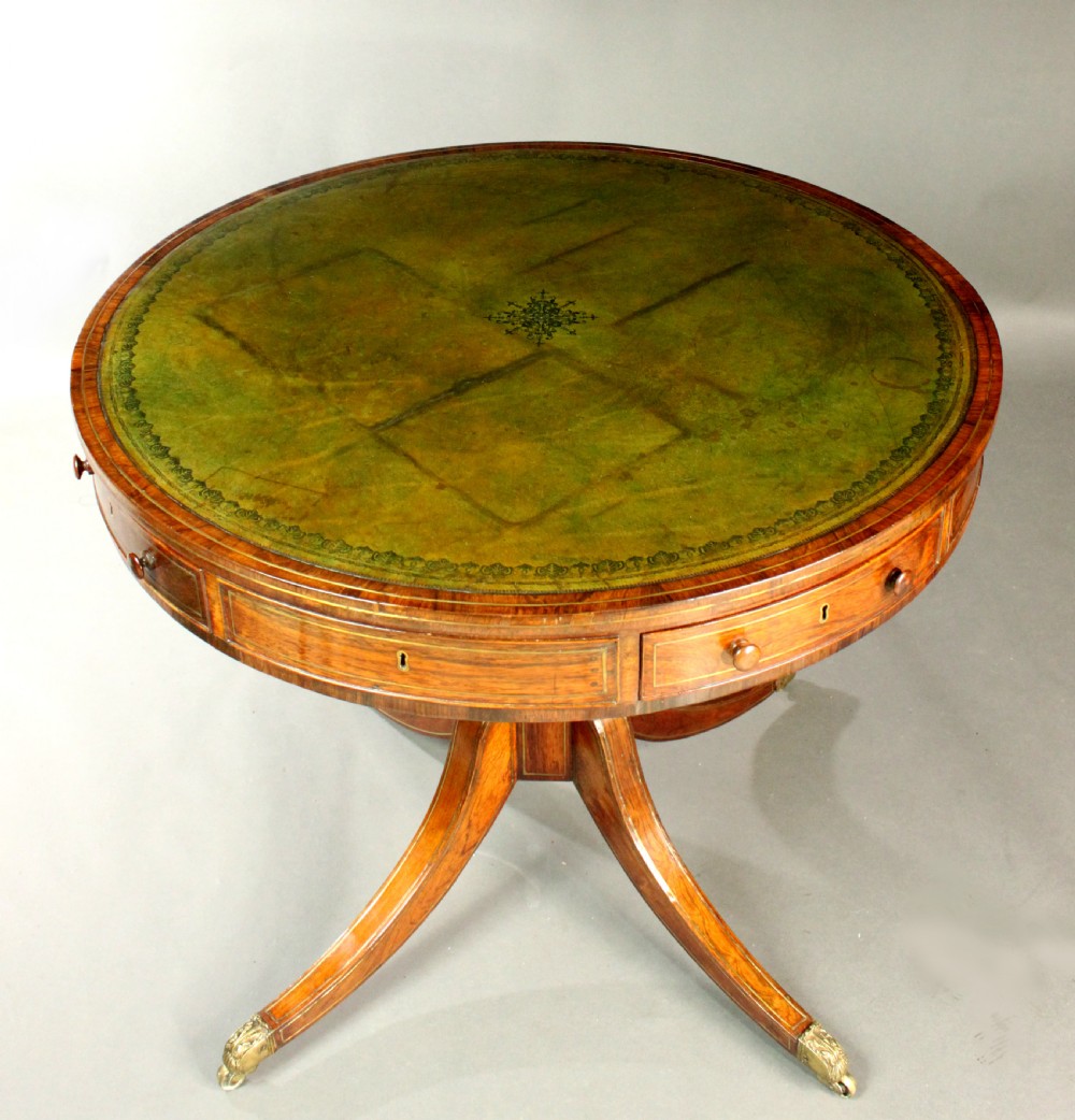 A circular Regency rosewood drum table with a green leather top, frieze drawers, and a central pedestal resting on four splayed legs with brass castors. View IV