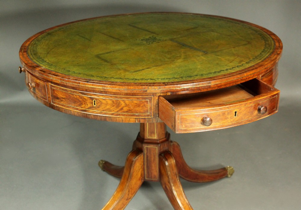A circular Regency rosewood drum table with a green leather top, frieze drawers, and a central pedestal resting on four splayed legs with brass castors. View V