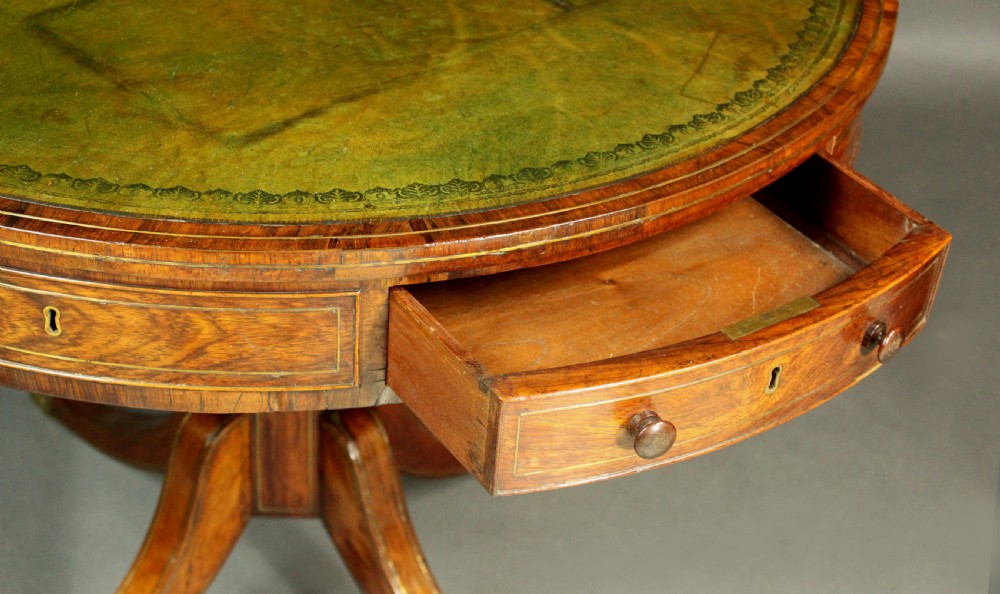 A circular Regency rosewood drum table with a green leather top, frieze drawers, and a central pedestal resting on four splayed legs with brass castors. View VI