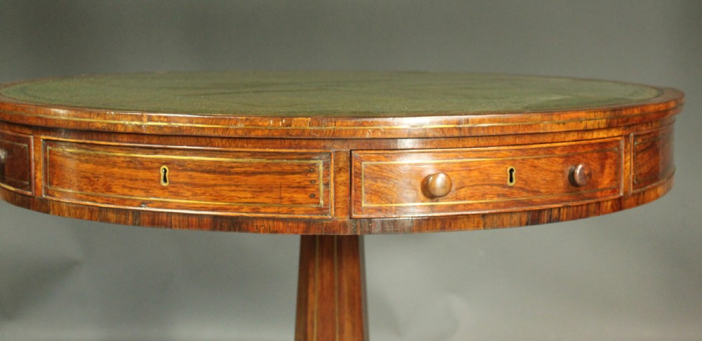 A circular Regency rosewood drum table with a green leather top, frieze drawers, and a central pedestal resting on four splayed legs with brass castors. View VII
