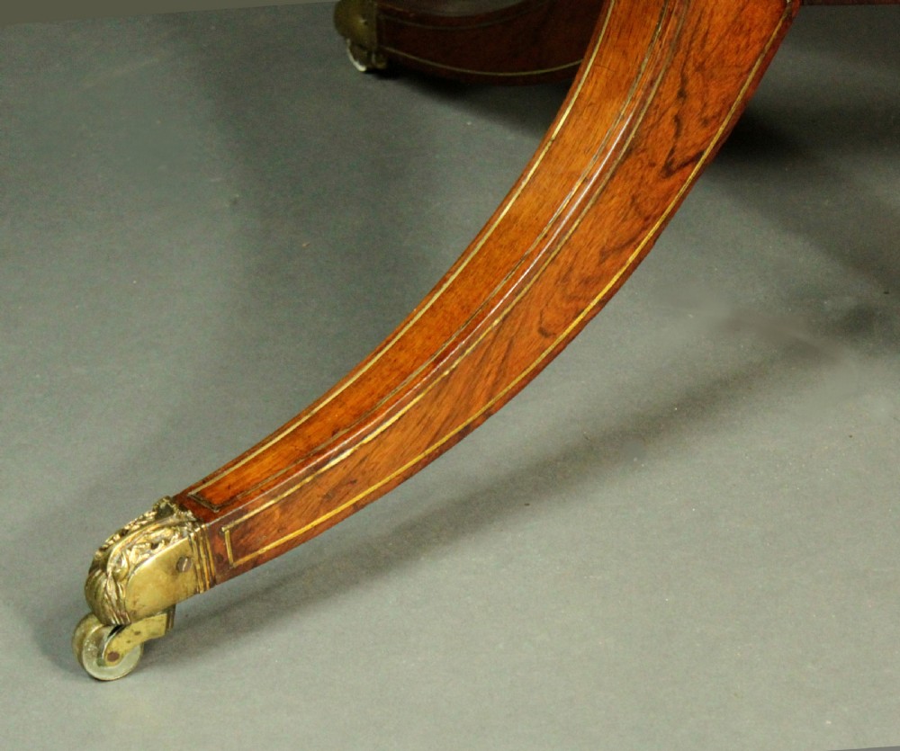 A circular Regency rosewood drum table with a green leather top, frieze drawers, and a central pedestal resting on four splayed legs with brass castors. View VIII