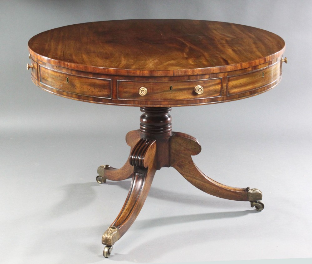 A circular Regency mahogany drum table featuring a deep drawer frieze on a turned central pedestal with four splayed legs and brass castors.