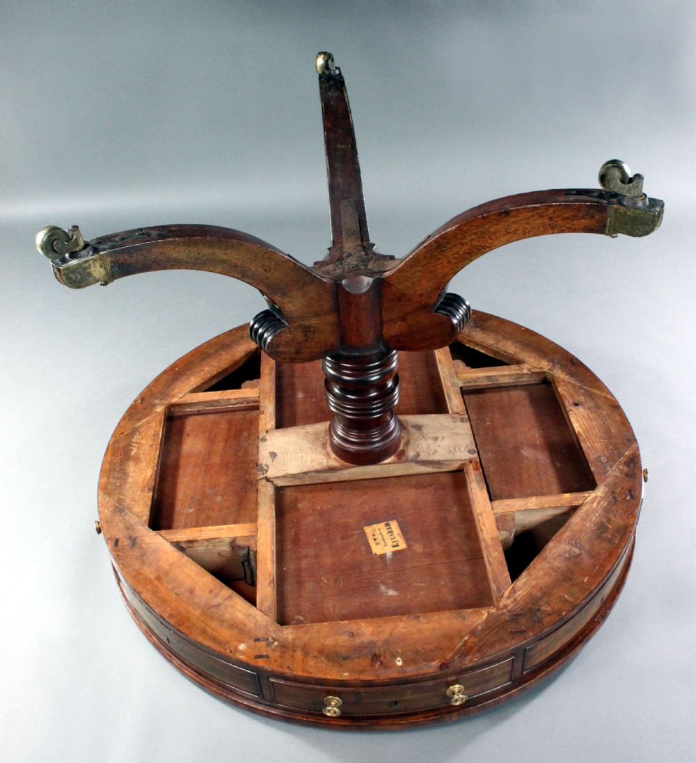 A circular Regency mahogany drum table featuring a deep drawer frieze on a turned central pedestal with four splayed legs and brass castors. View IV