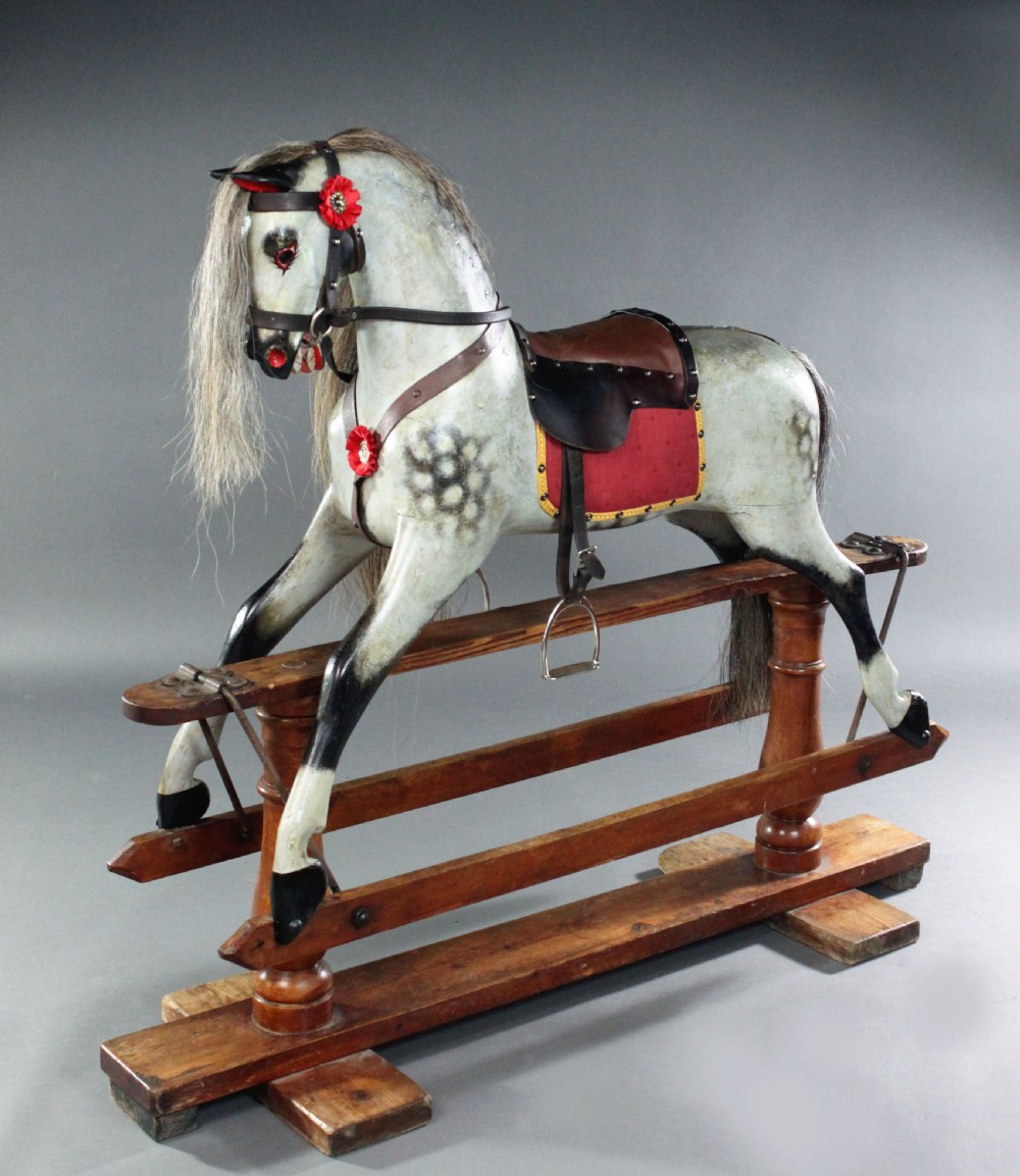 A 19th-century carved wooden dapple grey rocking horse mounted on a stained timber safety glider stand with leather tack and a natural horsehair mane.