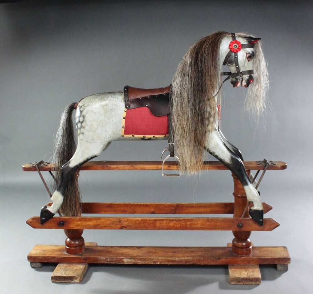A 19th-century carved wooden dapple grey rocking horse mounted on a stained timber safety glider stand with leather tack and a natural horsehair mane. View V