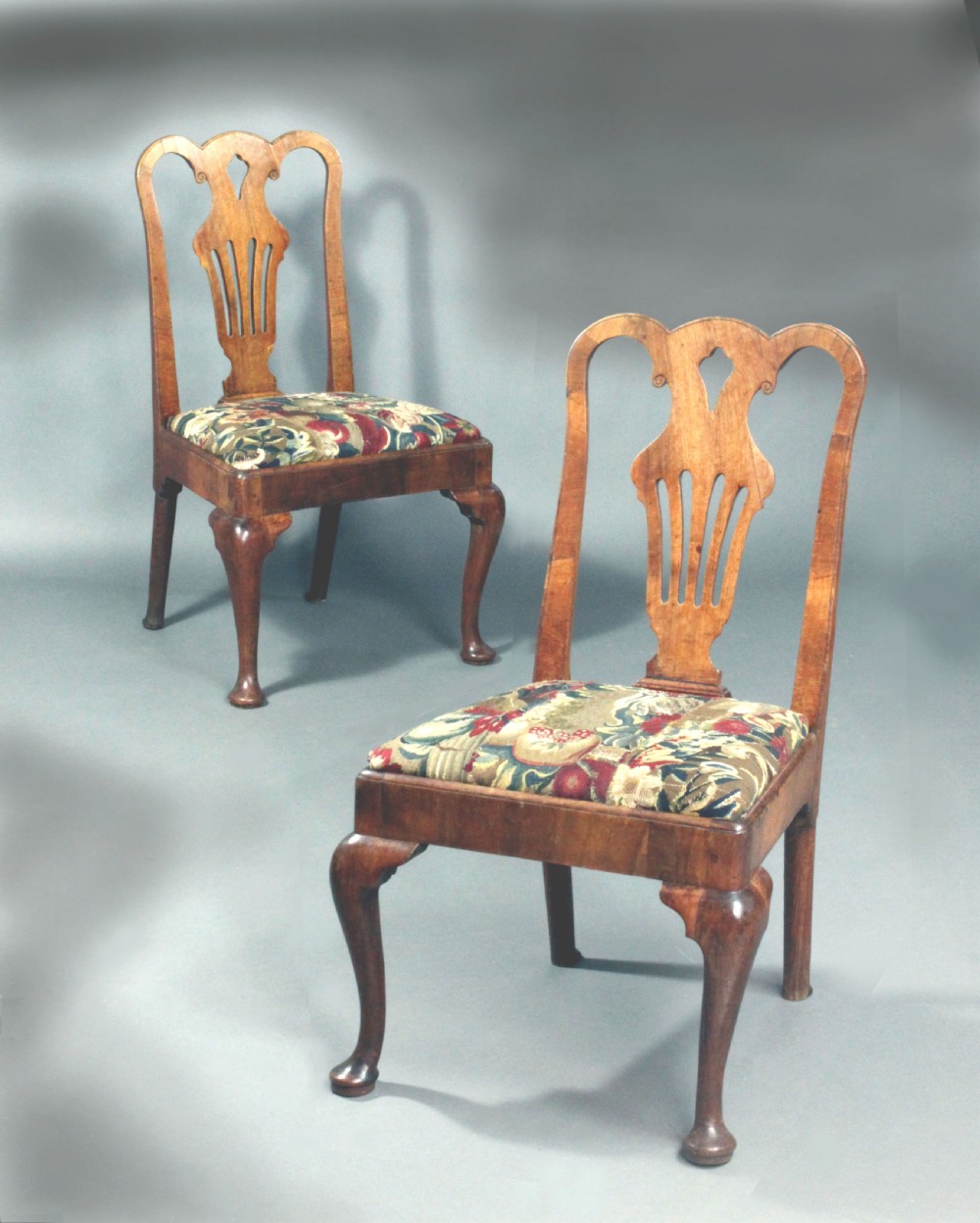 A pair of 18th-century George II walnut side chairs featuring pierced vase-shaped splats, floral upholstered drop-in seats, and front cabriole legs.