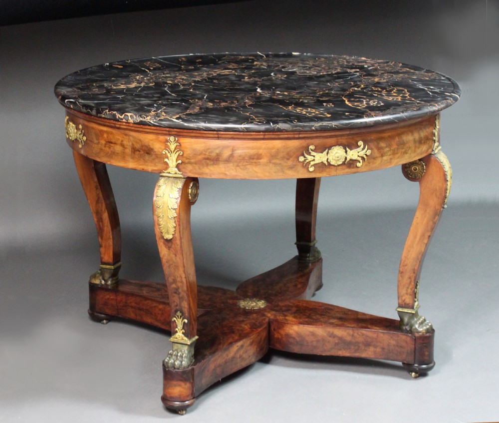 A circular French Empire centre table featuring a black veined marble top, mahogany apron with gilt bronze mounts, and curved legs on a cruciform base. View II