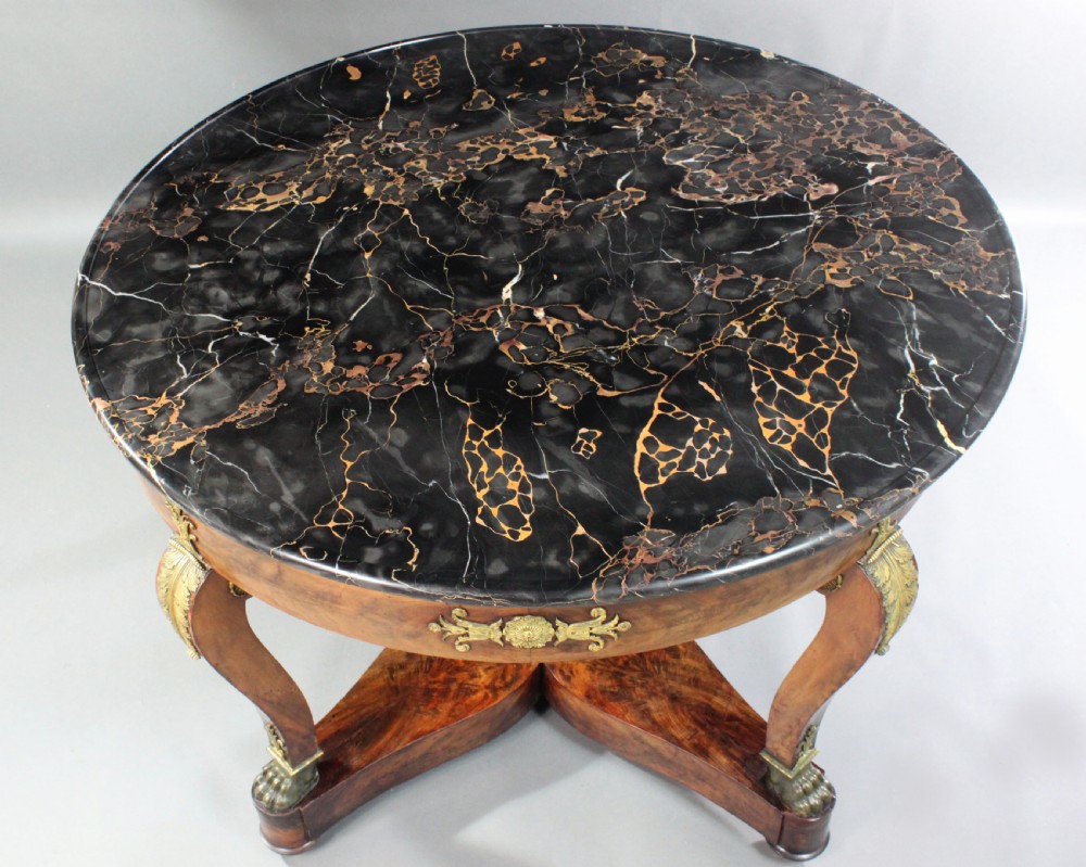 A circular French Empire centre table featuring a black veined marble top, mahogany apron with gilt bronze mounts, and curved legs on a cruciform base. View III