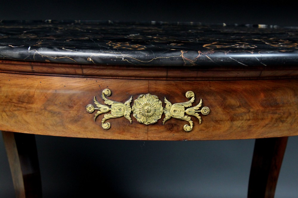 A circular French Empire centre table featuring a black veined marble top, mahogany apron with gilt bronze mounts, and curved legs on a cruciform base. View VII